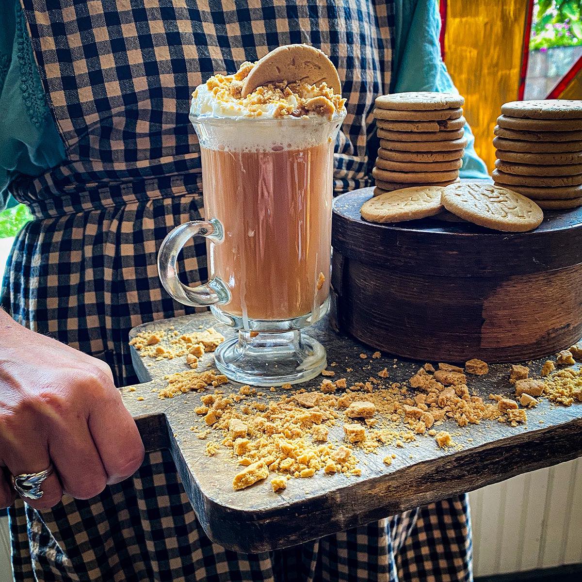 A woman carries a tray with crumbled cookies surrounding a brewed mug of Gingersnap Tea.