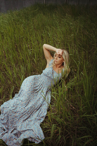 Woman laying in field modeling the Floral Tiered Maxi Dress.  The dress is Slate Grey with floral colors of blues and orange. 