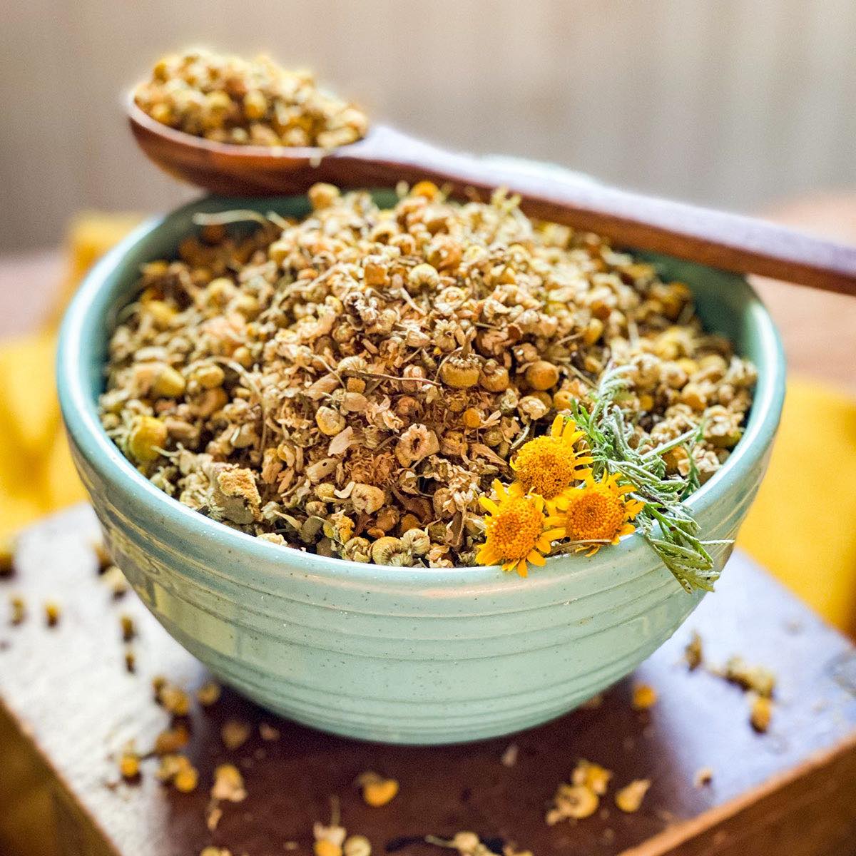 Dried chamomile flowers in a green bowl with a wooden spoon