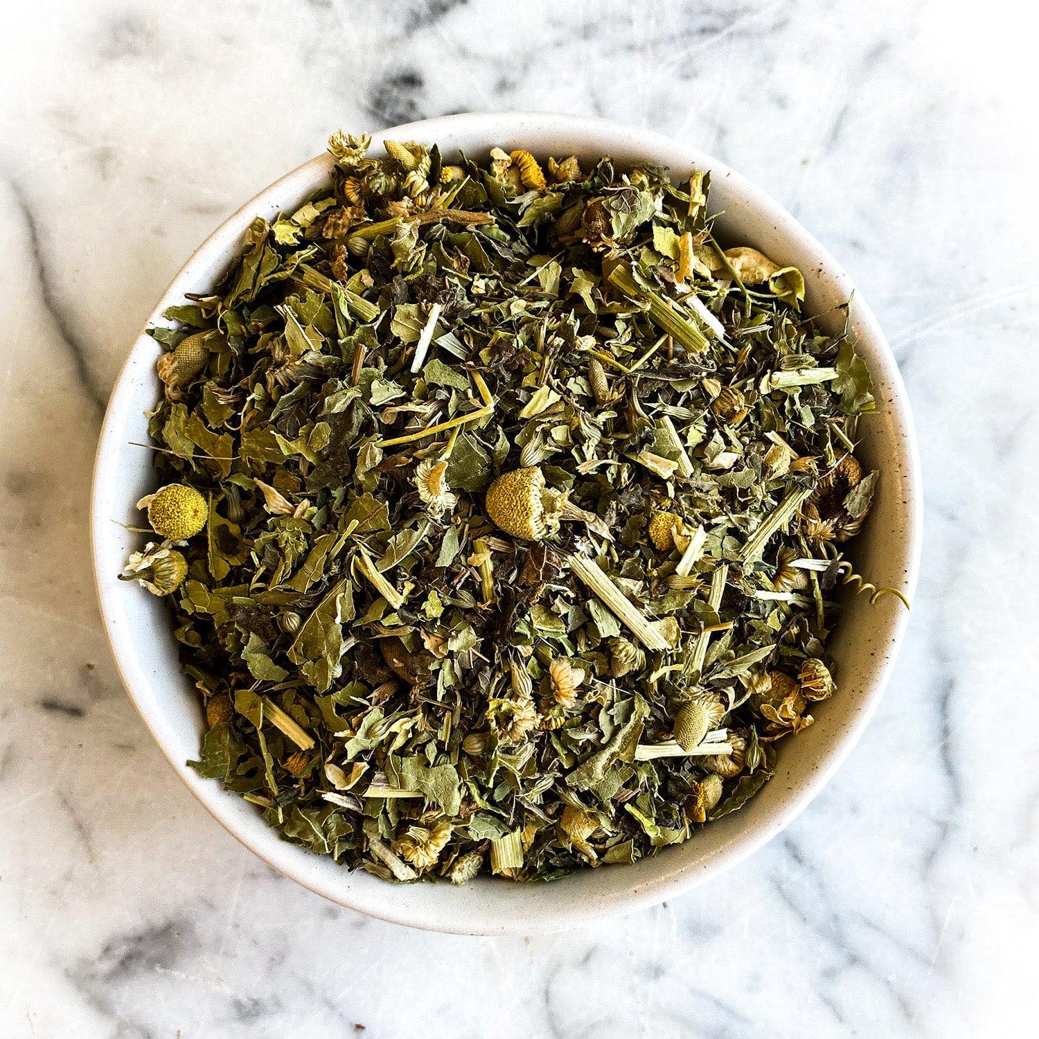 A bowl filled with dried Fast Asleep Tea rests on a white, marble tabletop.
