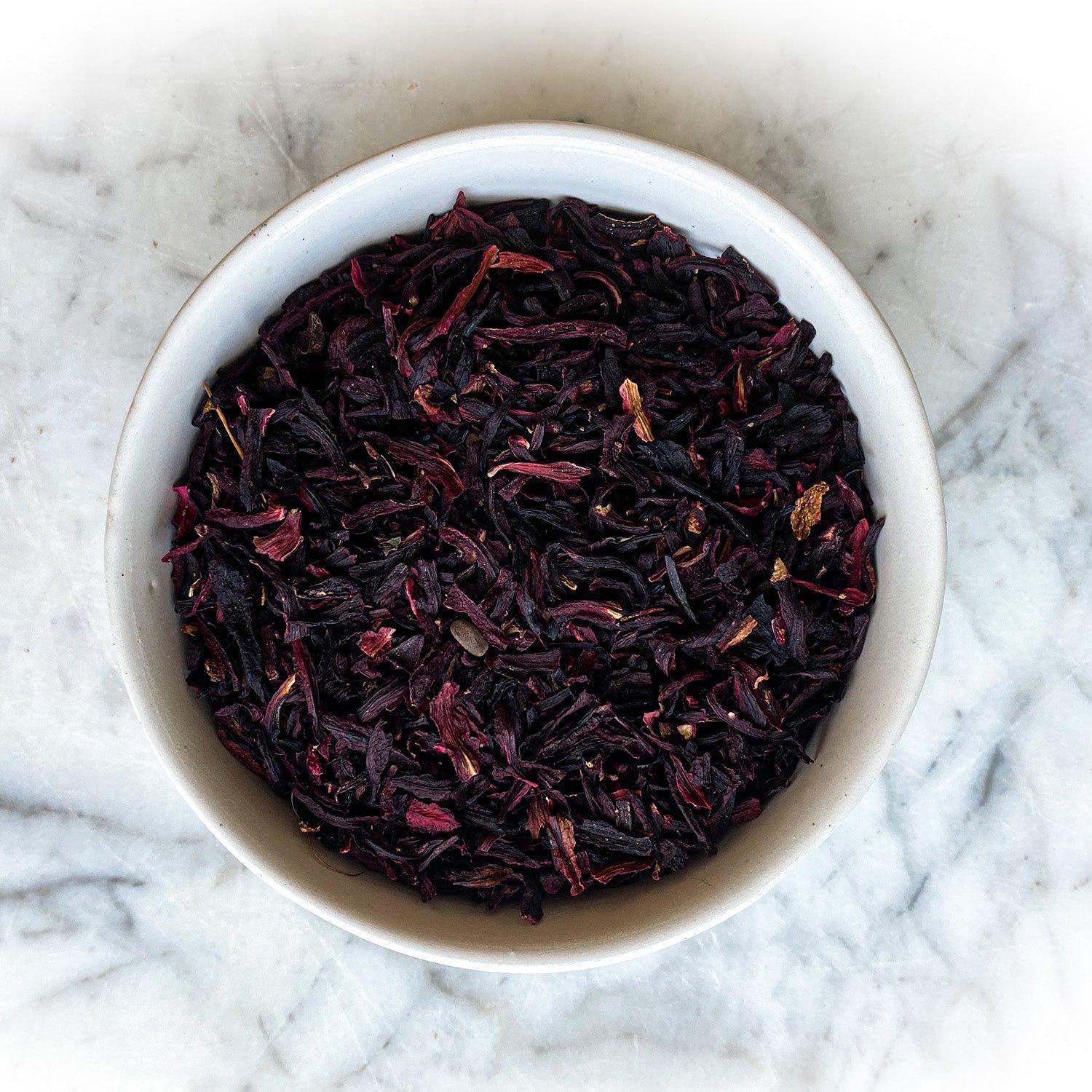 Dried hibiscus flowers in a white bowl on a white marble background