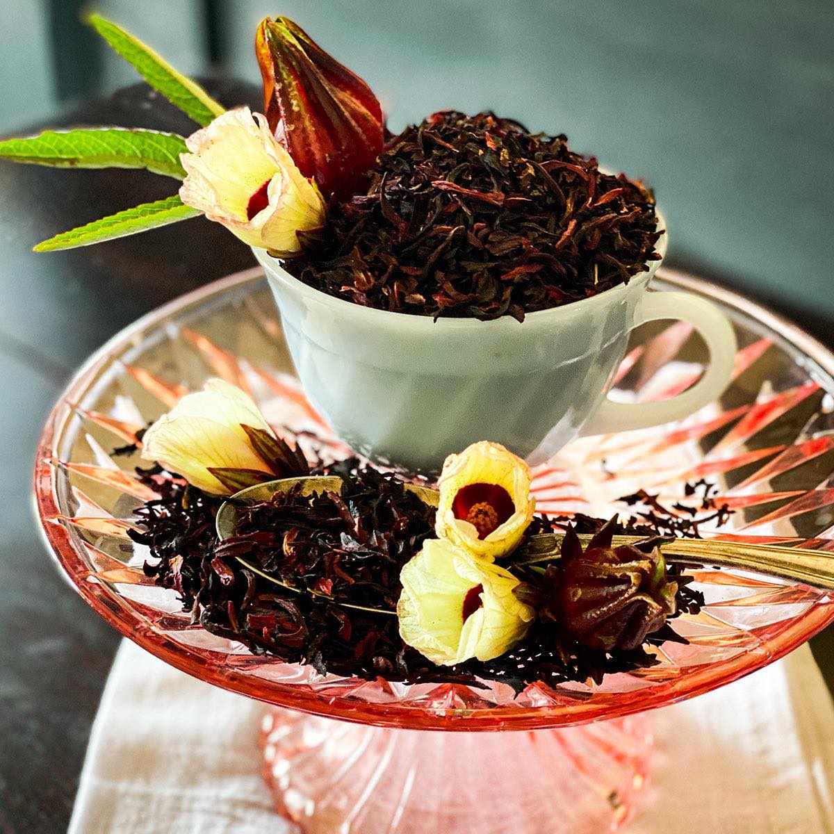 Dried hibiscus flowers in a white mug with fresh hibiscus flowers in the foreground