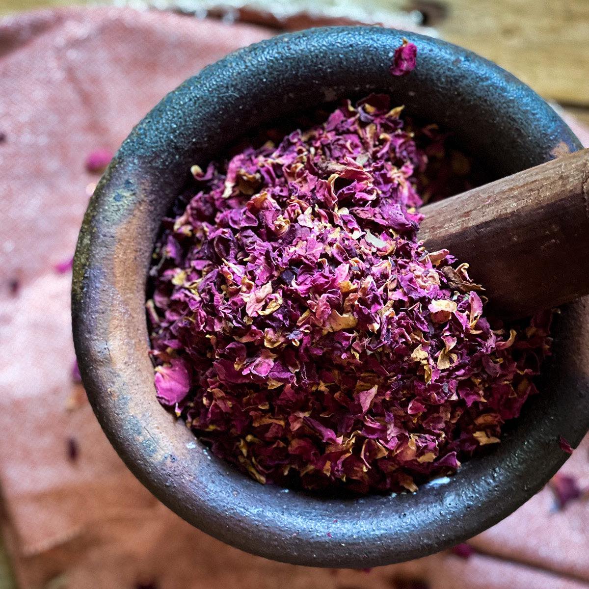 Dried red rose petals in a mortar with a pestle.