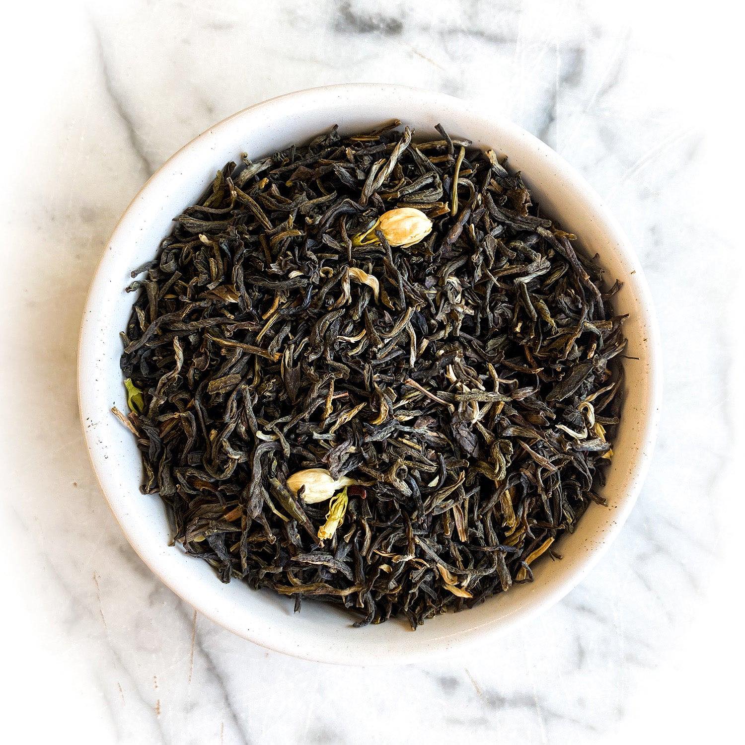 Dried Jasmine Green tea in a white bowl on a white marble table.