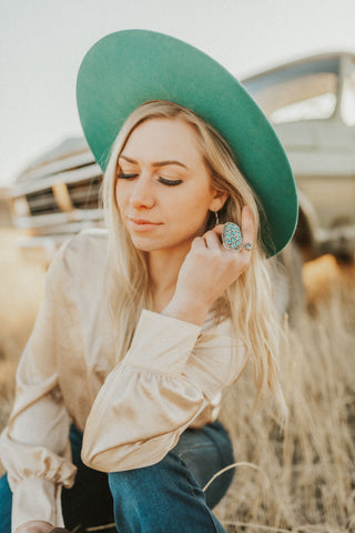 Woman sitting in field wearing the TeePee Teal Cowgirl Hat by Charlie 1 horse. 