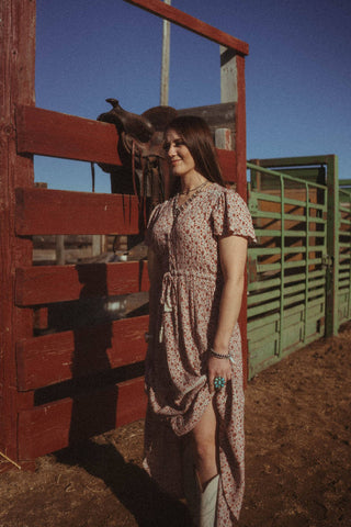 Woman standing in corral modeling the Prairie Dress by Cotton & Rye.  The Dress features a tassle in front of waist. .