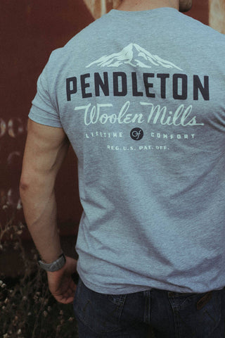 Man modeling back side of the pendleton gray shirt with Pendleton logo written across top and the words Woolen Mills underneath featuring picture of mtn peak.
