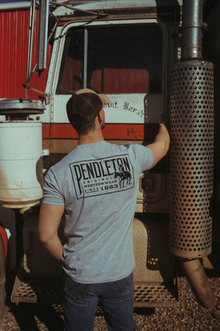 Man standing near semi modeling back of the Woolen Mills shirt.  The back has Pendleton written across back and man on horse.  