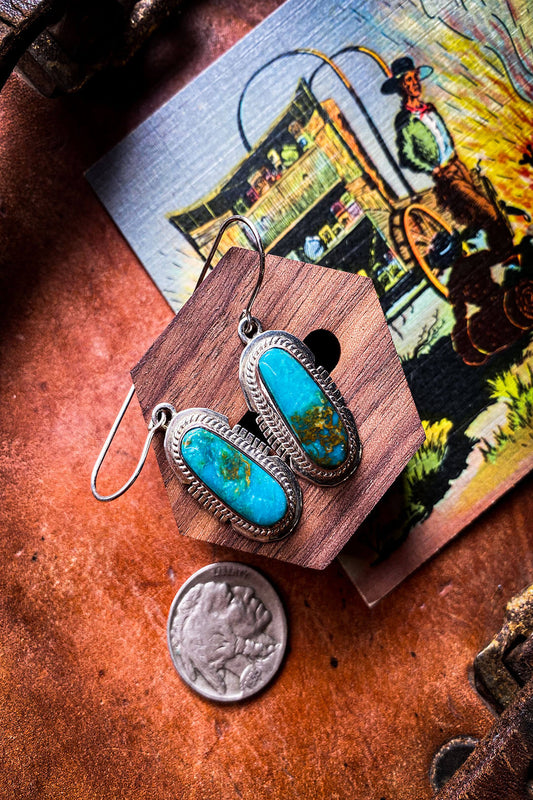 Pilot mountain turquoise earrings in a sterling setting lay on a piece of leather.