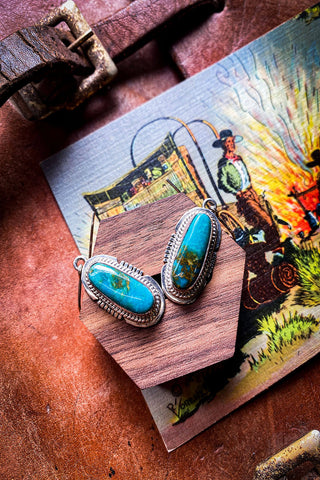 Pilot mountain turquoise earrings rest on piece of wood.