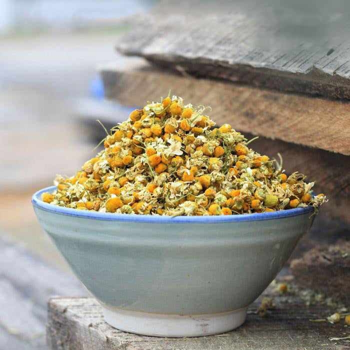 Chamomile flowers overflowing out of a light blue and white bowl set on a pile of wood.