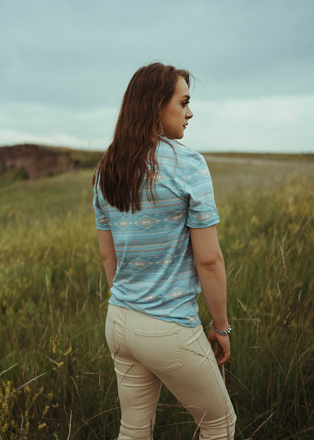 Woman modeling the back of the All Over Print Tee in Aqua. Aztec Design