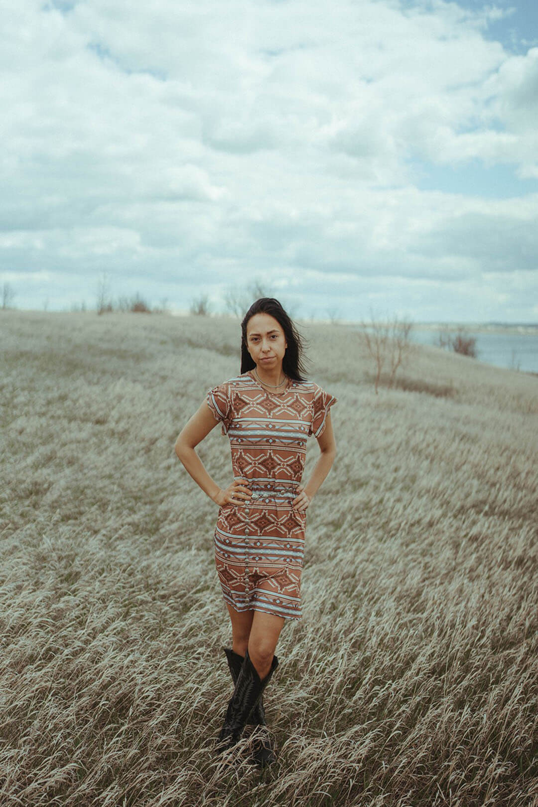 Woman standing in field wearing the Camel Aztec Ribbed Dress.  The dress is more fitted and comes just above the knee.  