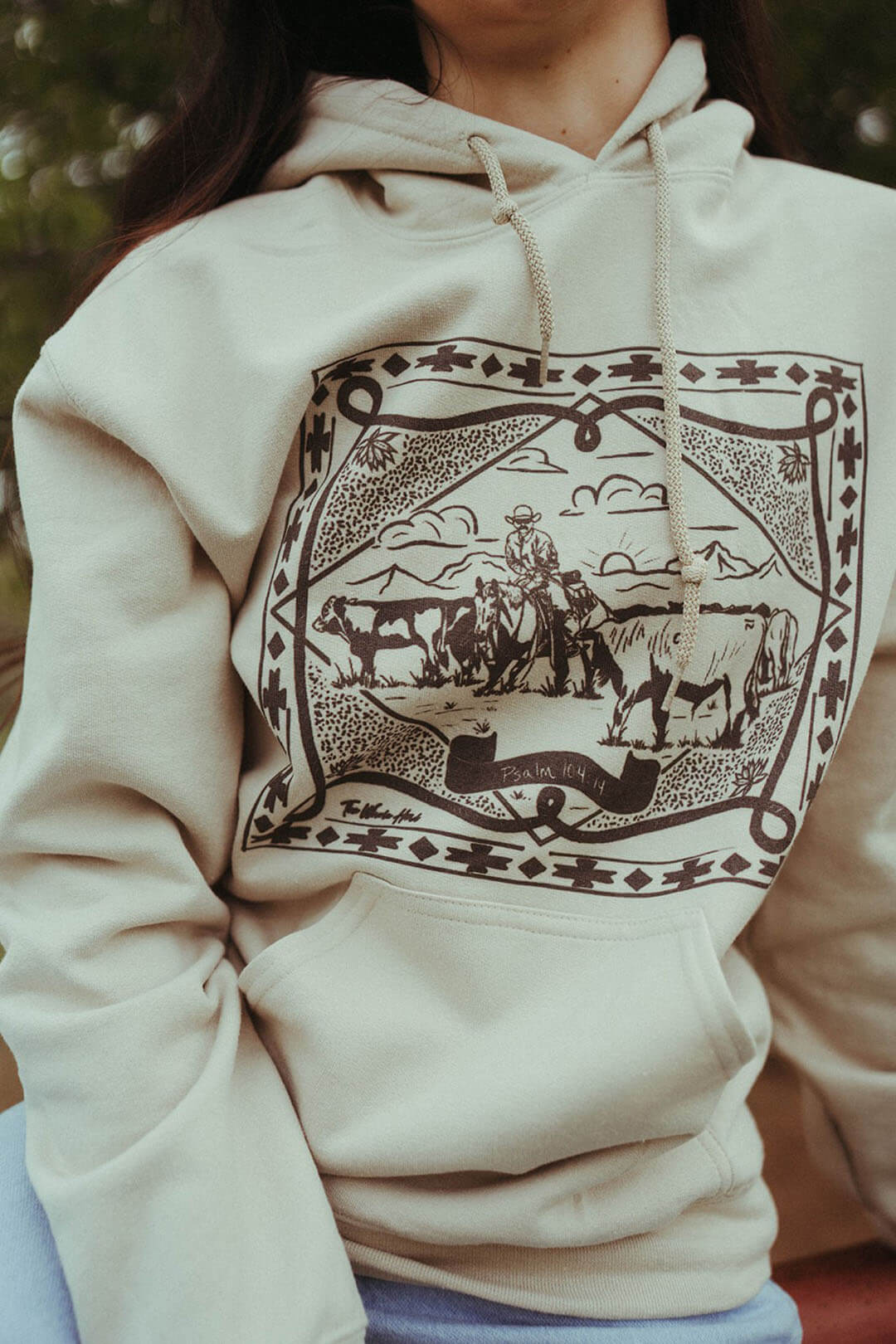 Woman wearing Pslam 104:14 Hoodie by The Whole Herd.   Scene of man riding horse with cows.