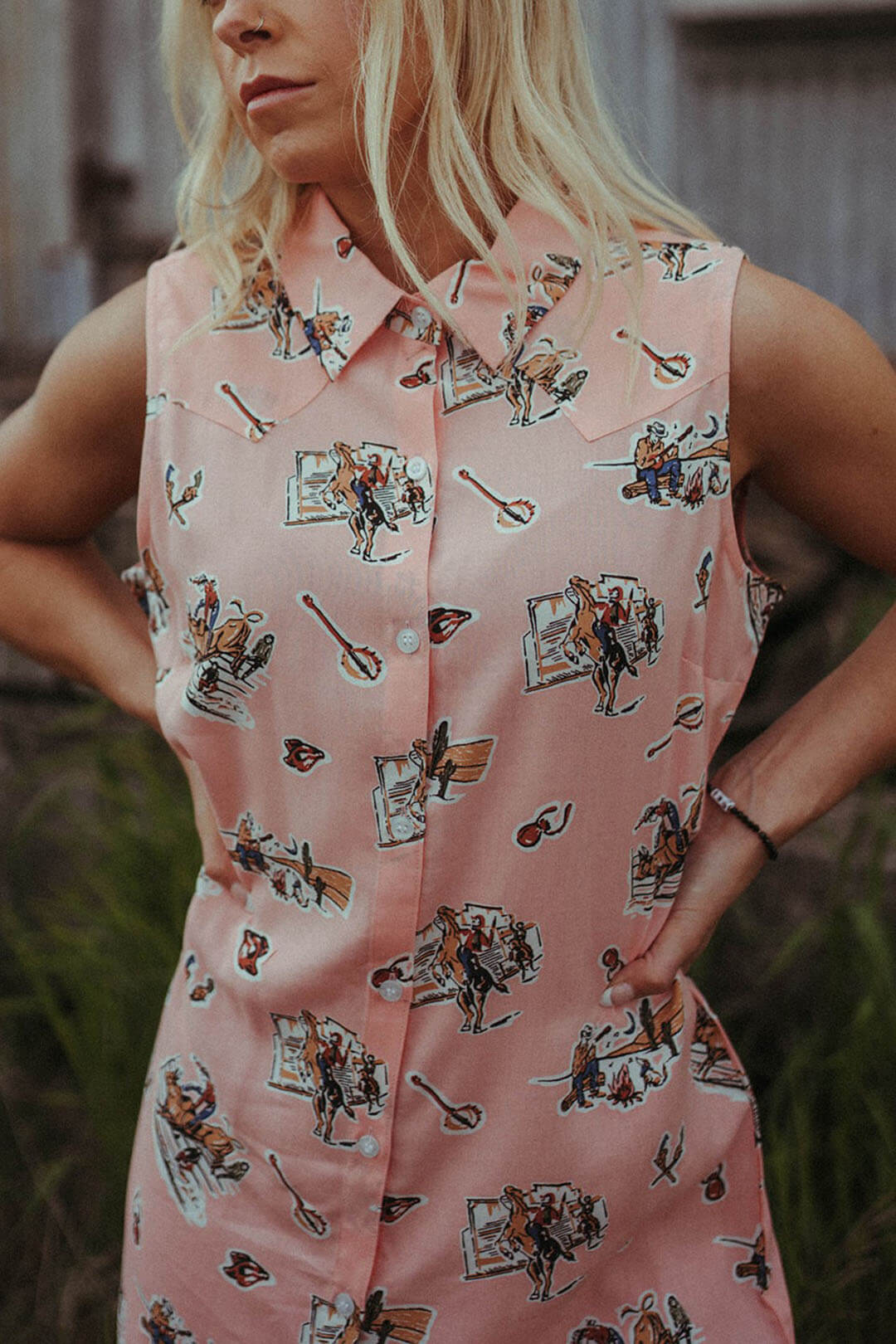Close up image of the Sleeveless Cowboy Print Duster/ Dress by Rock & Roll Denim.  Pink in color with western scene graphics.