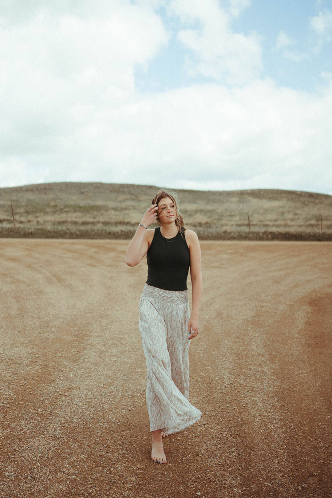 Woman standing on dirt road wearing the Smocked Waist Maxi Pants.  They have an elastic waist. 