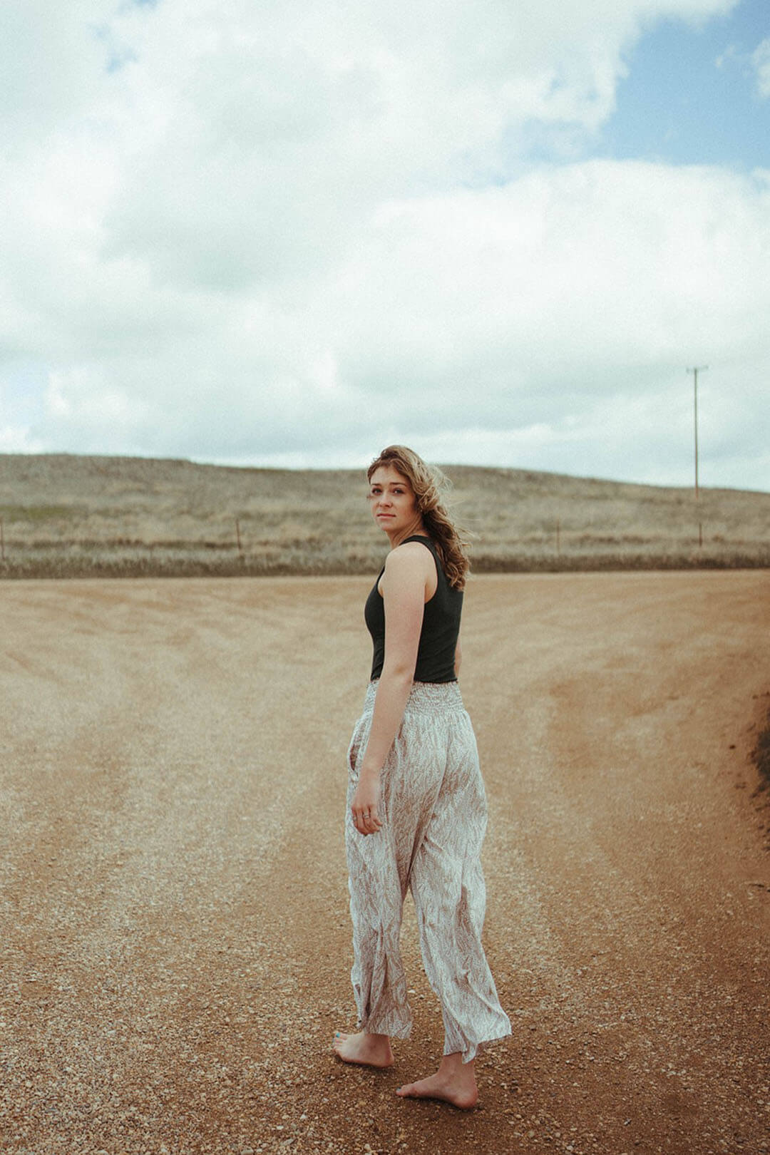 Woman standing on dirt road modeling the Smocked Waist Maxi Pants.  Brown and white color.