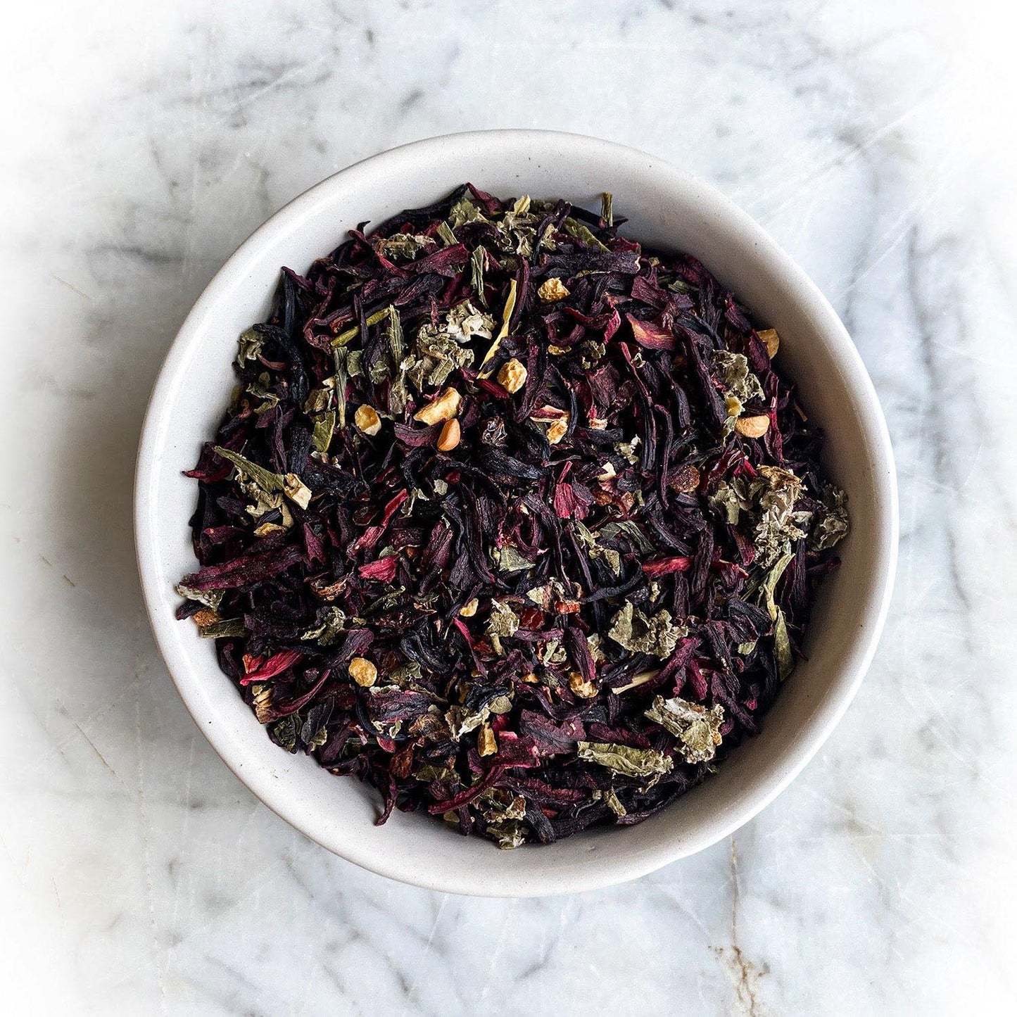Dried Hibiscus Orange Delight Tea in a white bowl on a white marble table.