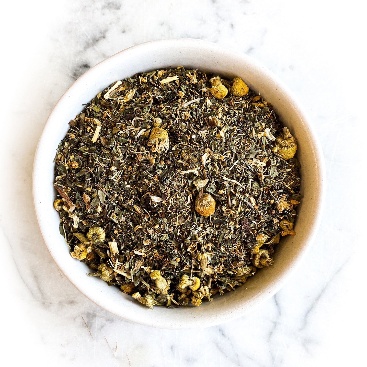 Dried Cold Comfort Tea in a white bowl on a white marble  countertop is the focus of this photo.
