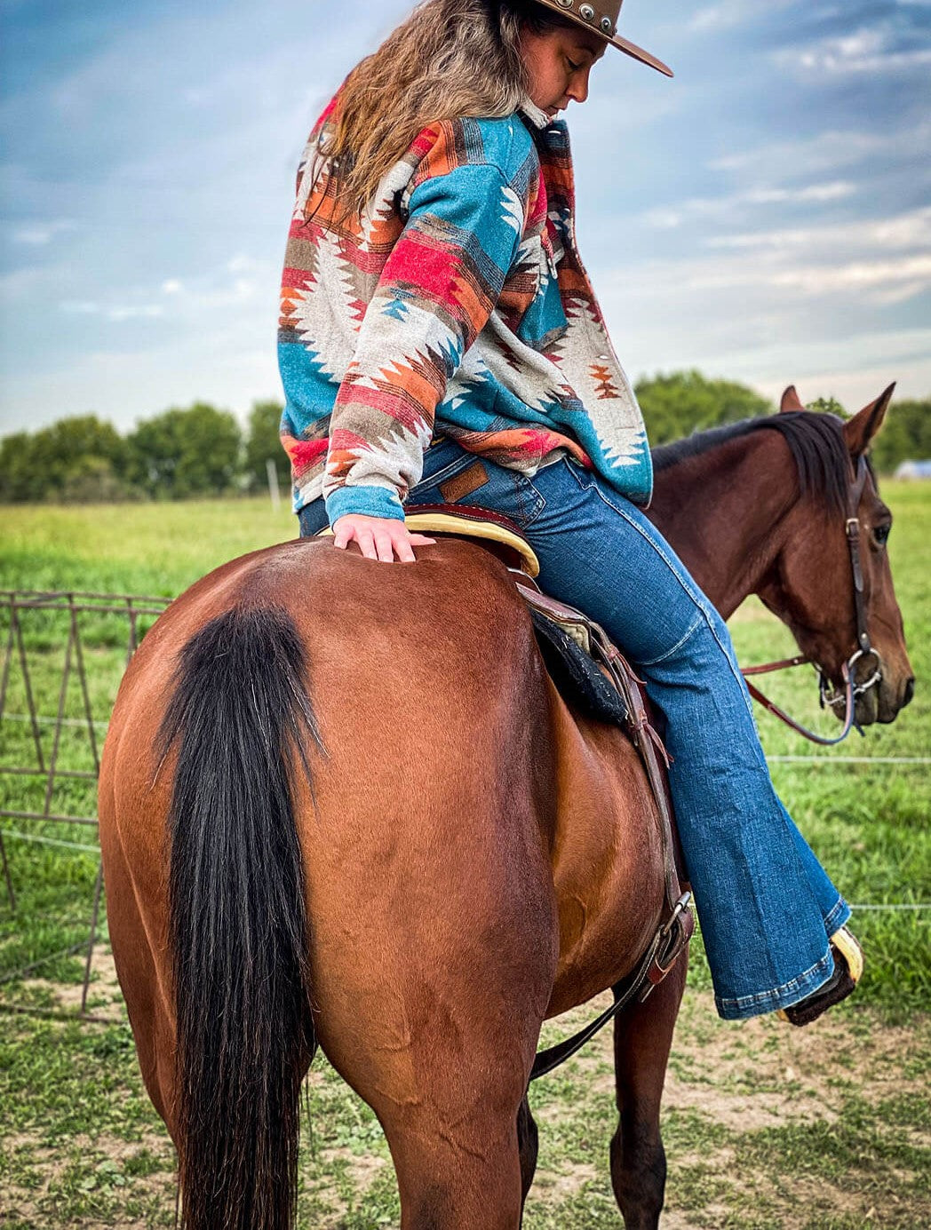 Woman riding horse modeling the back of  the Aztec Jacket by Jodifil.  Features colros of orange, red and blues.  