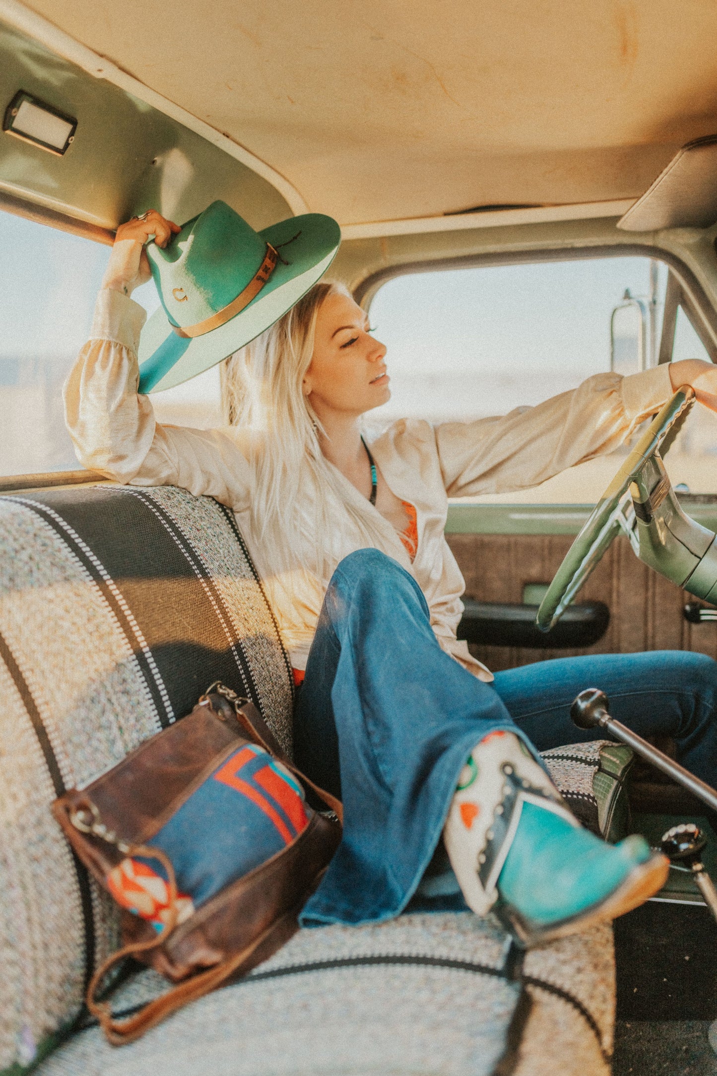 Woman sitting inside truck putting on the TeePee 78 Cowgirl Teal hat.  The hast is teal colored and has leather band around it. 