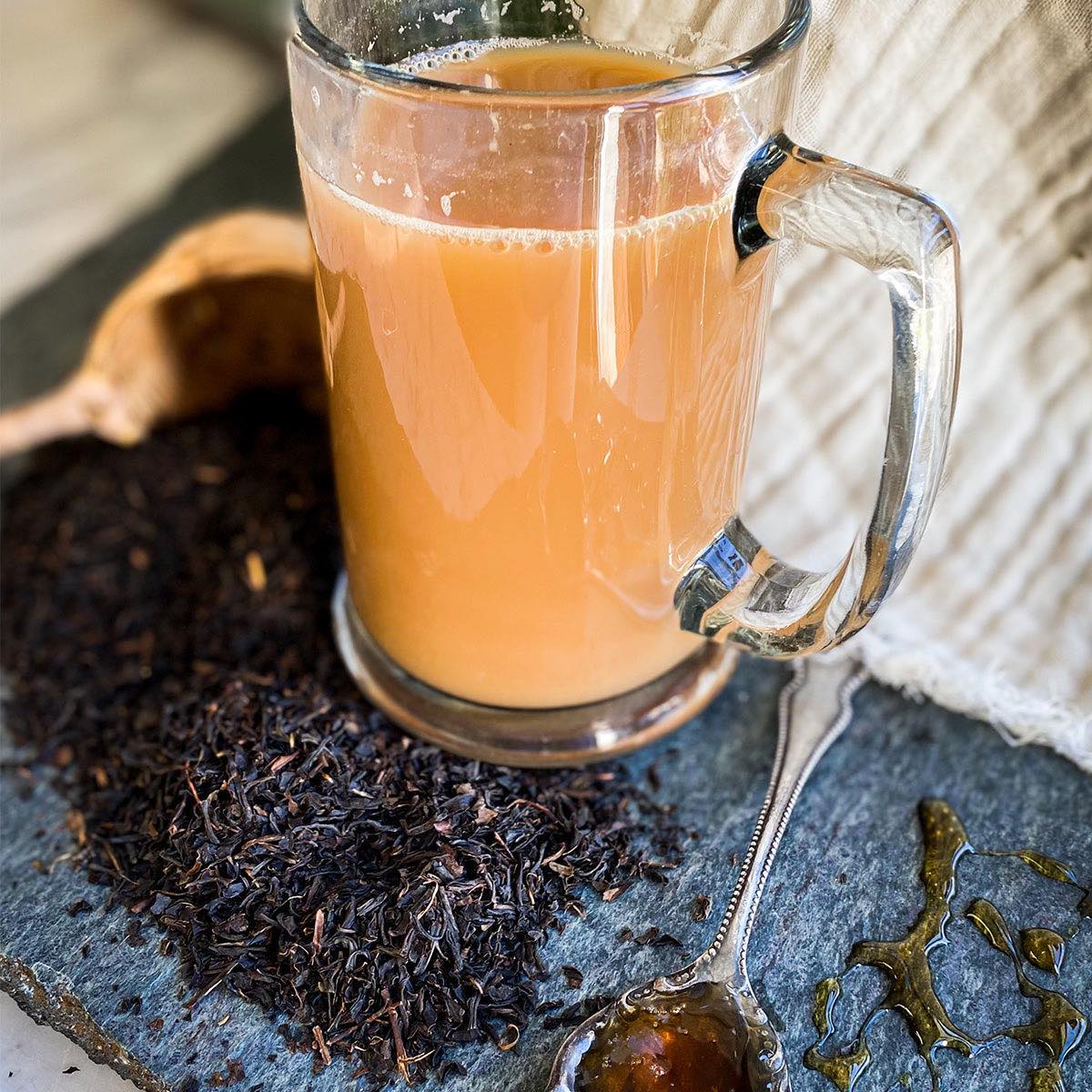 Brewed black keemun tea with cream in a glass mug with the dried tea surrounding it on the table.