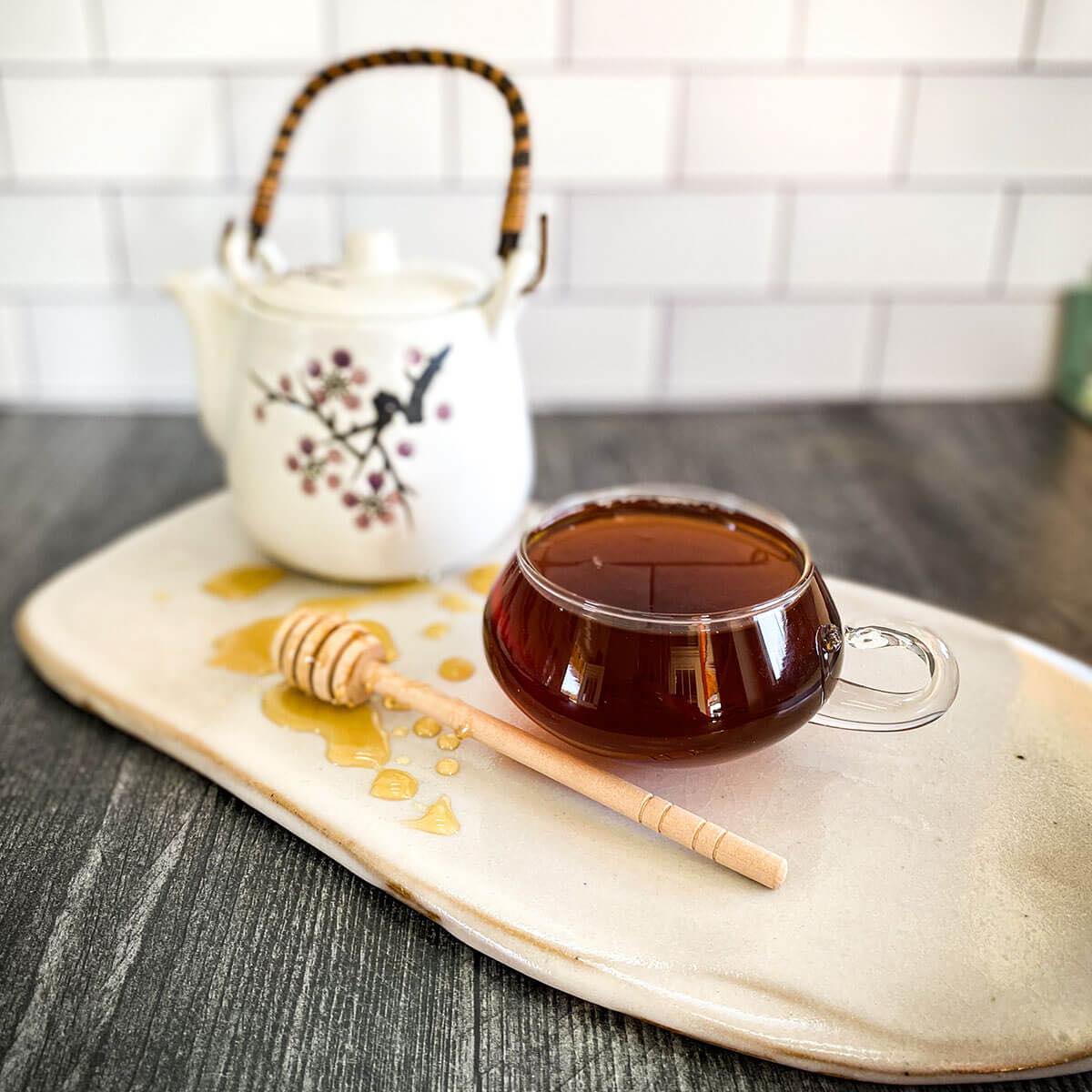 Brewed black spice chai tea in a glass mug with a white tea pot in the background.