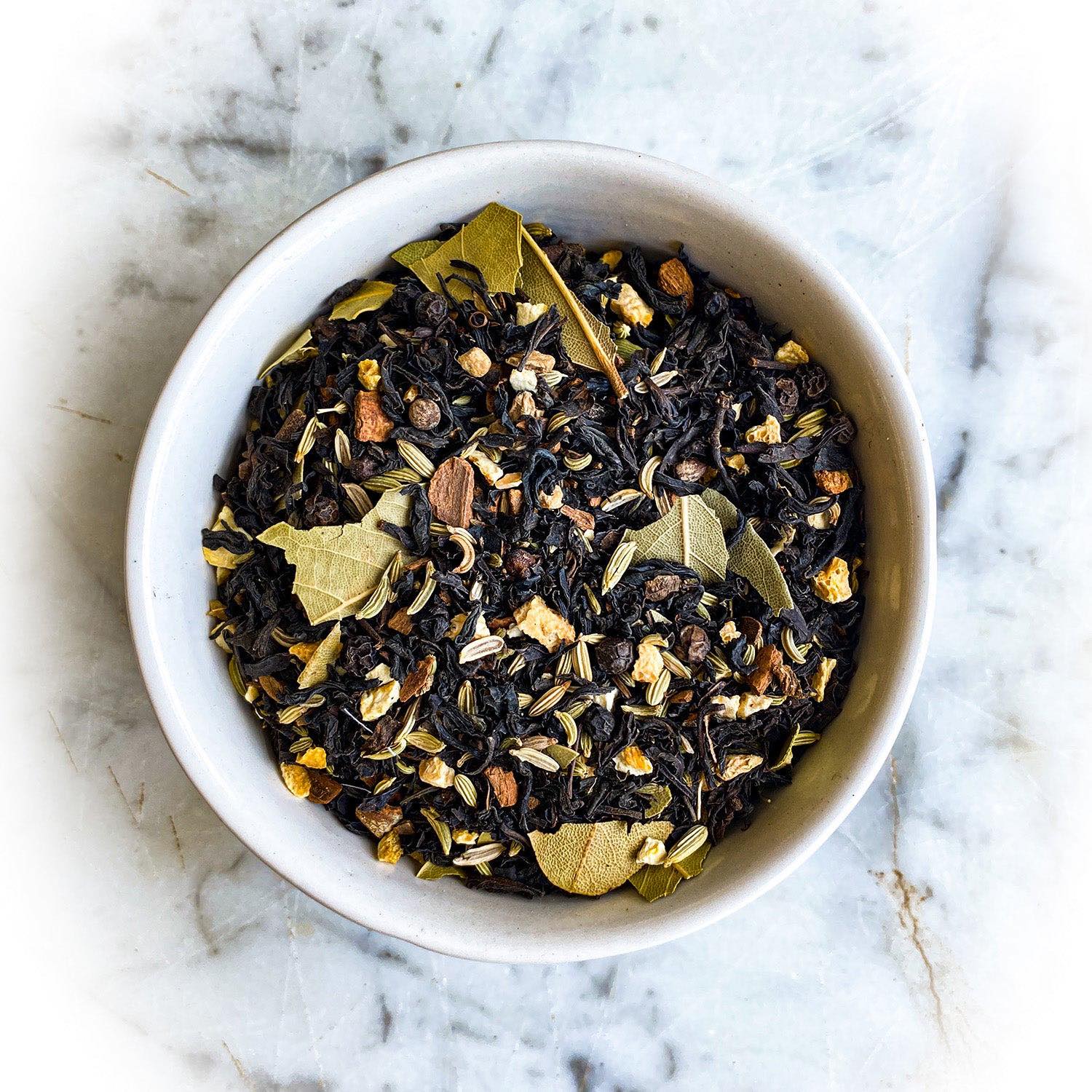 Black spice chai dried tea in a white bowl on a white marble table.