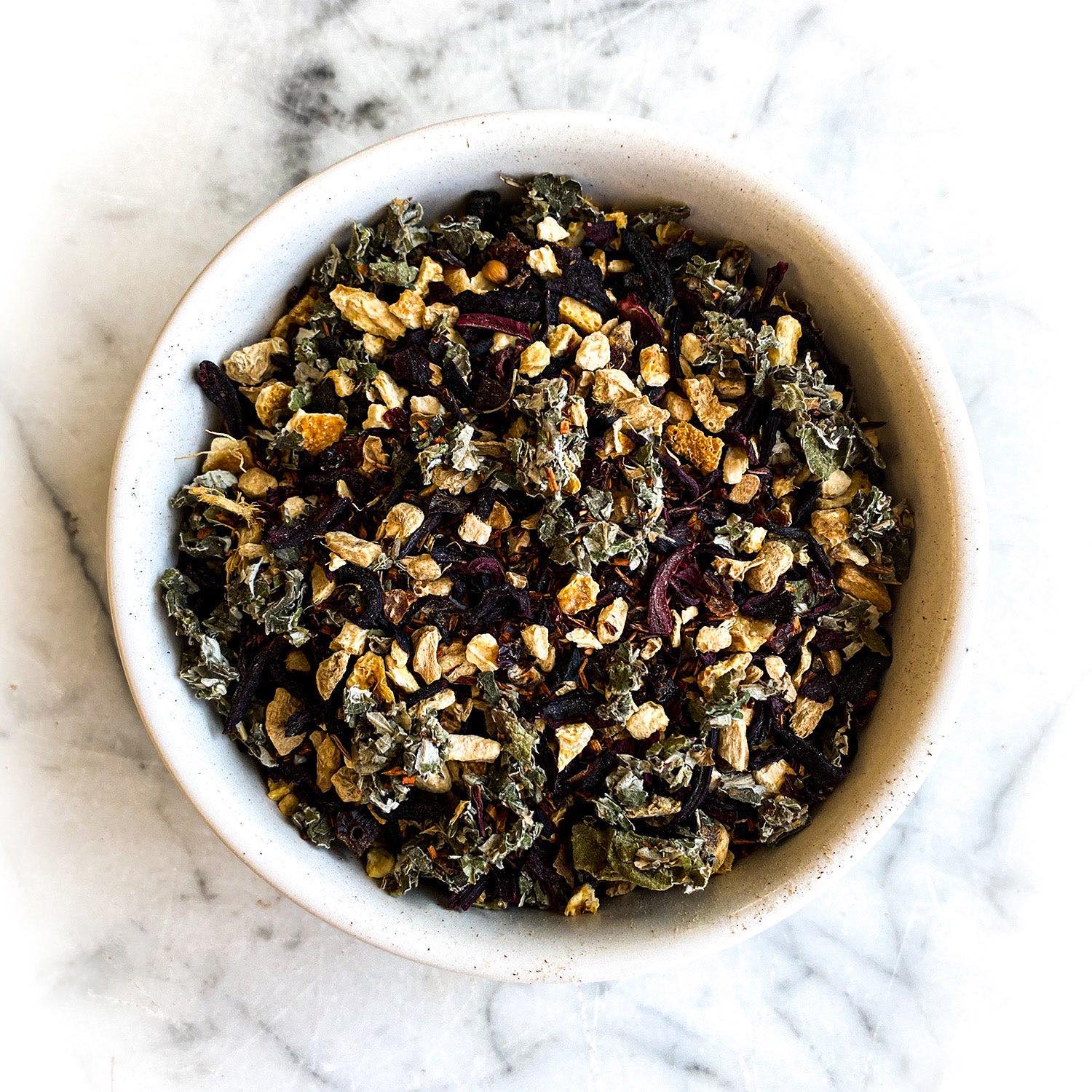 A white bowl filled with dried Herban C tea on a white marble surface.