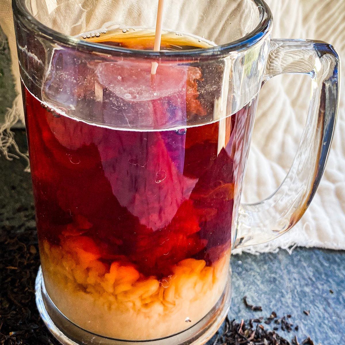 A glass mug filled with brewed black keemun tea while a stream of cream is being added.