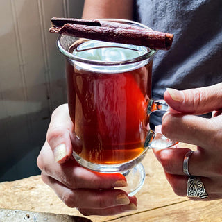 Brewed black spice chai tea with a cinnamon stick on top of the mug from a side view.