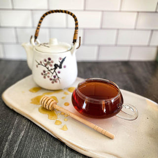 A brewed glass cup of Christmas Tea with a honey wand dripping with honey on the table and a white tea pot.