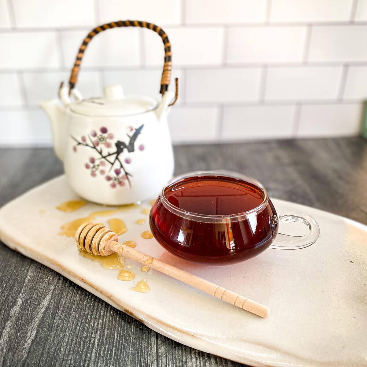 A brewed cup of Creamy Pumpkin Pie tea rests on a white ceramic surface with a honey wand and white tea pot.