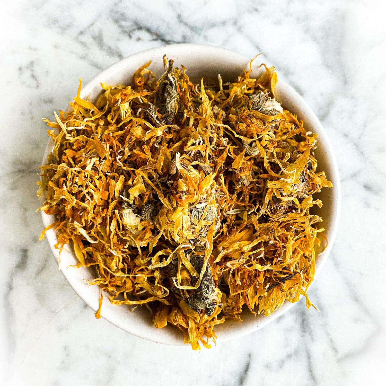 Calendula flowers in a white bowl on white marble