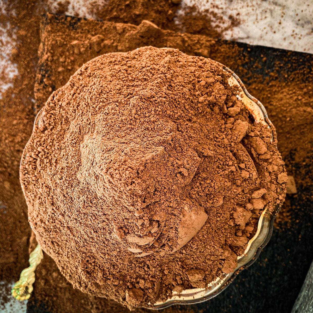 A silver dish is filled to overflowing with cacao powder.