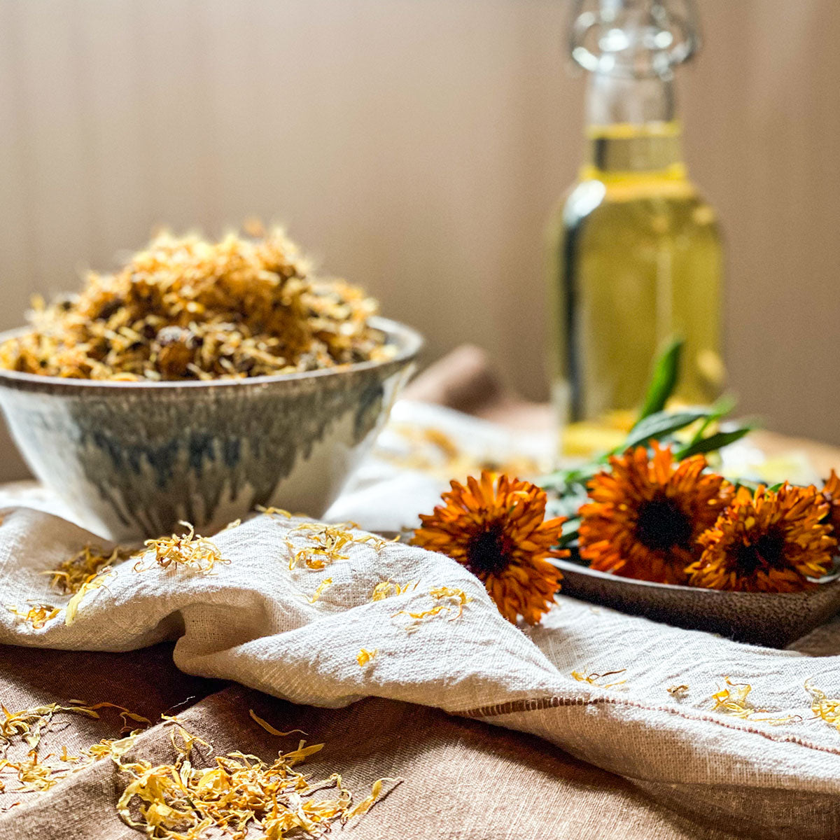 Calendula flowers in a bowl with a bottle of oil in the background and fresh flowers