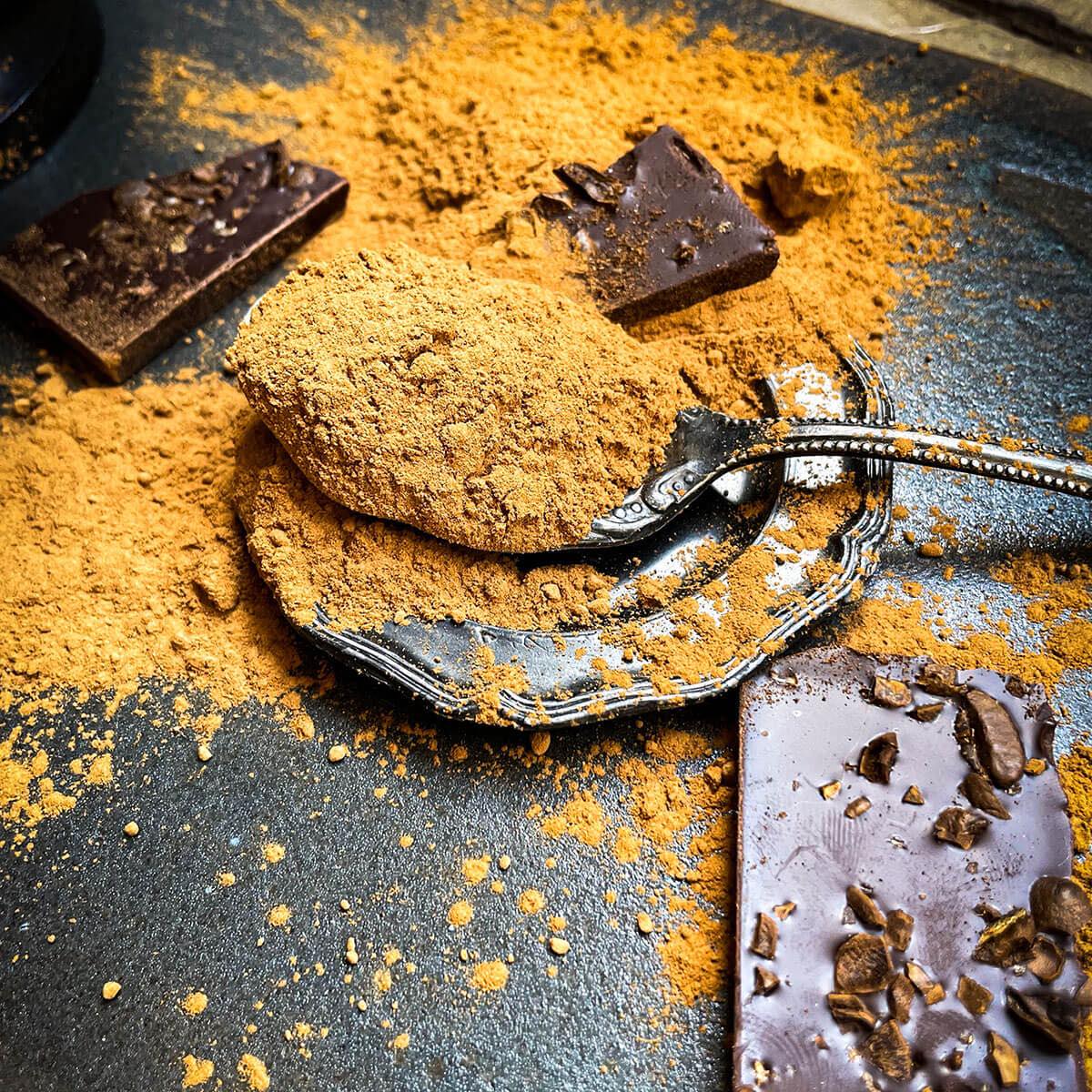 Carob powder in a spoon on a dark background with chocolate bars