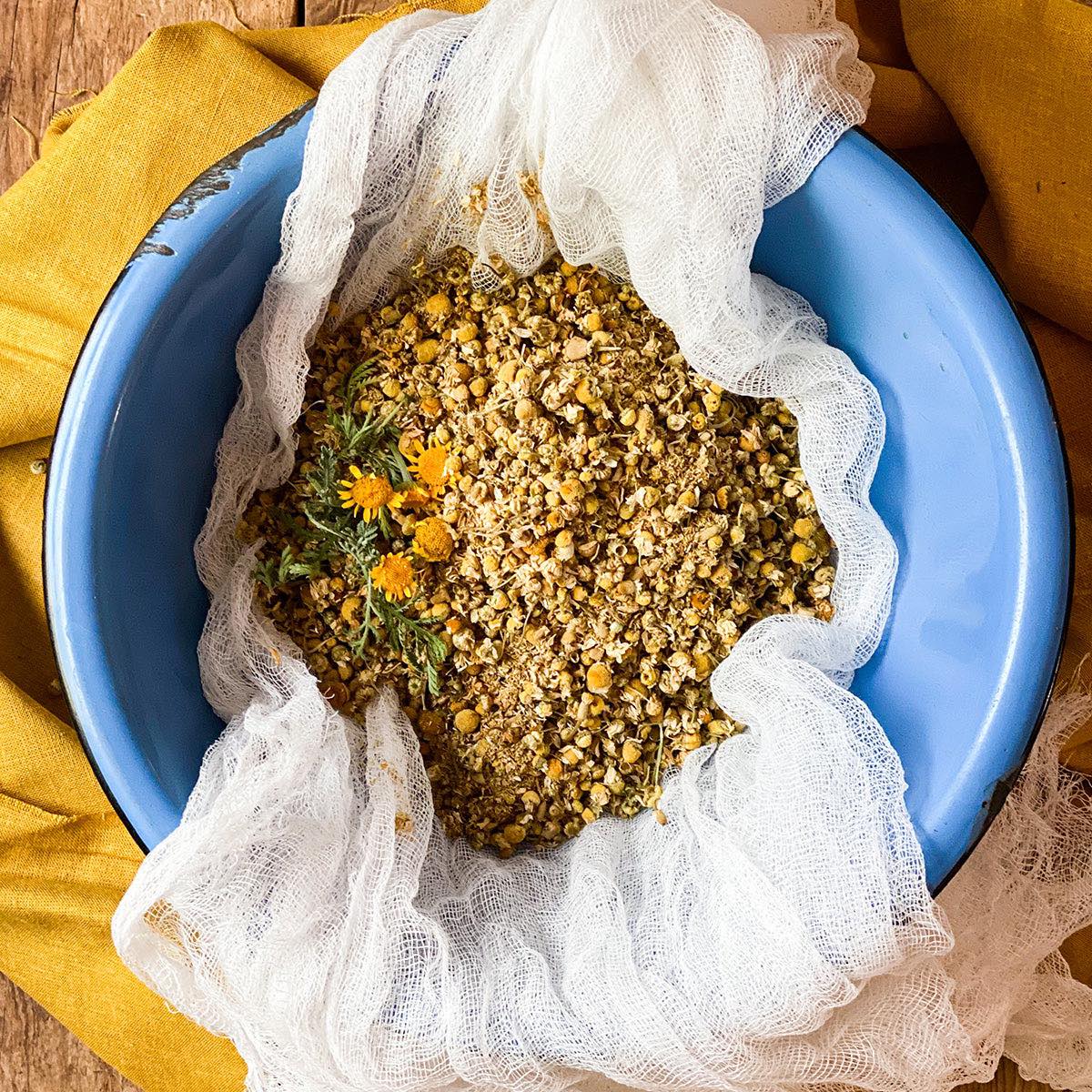 Dried chamomile in a blue enamel bowl with yellow linen fabric under the bowl