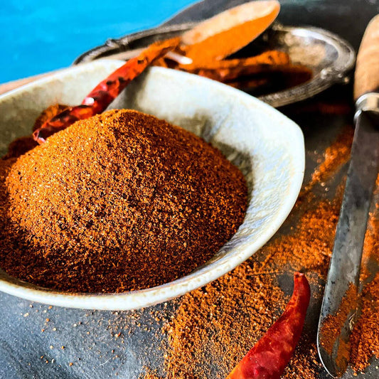 Chili powder seasoning blend in a white bowl with dried peppers