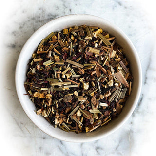 A white bowl is filled with dried Christmas Tea. The bowl sits on a white marble tabletop.