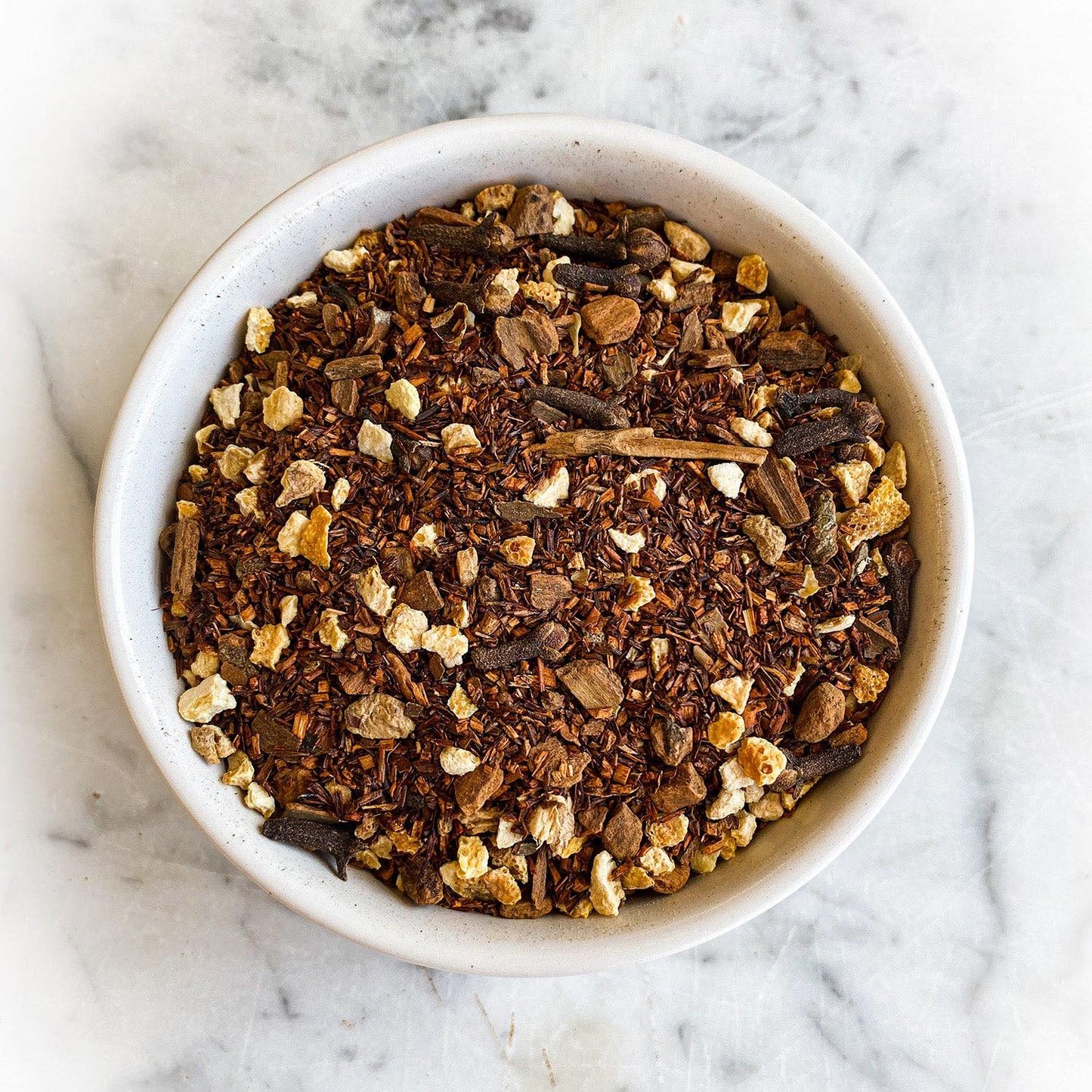A bowl of dried Creamy Pumpkin Pie tea sits on a white marble counter.