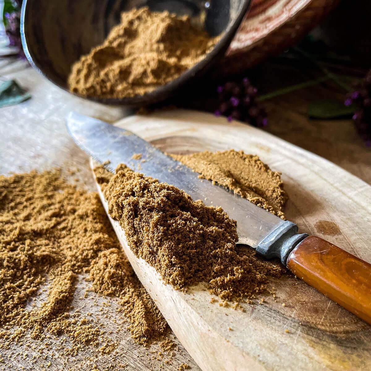 Cumin Seed Powder spills off a cutting board with a knife.