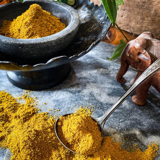 Curry powder is mounded in a stone bowl with a wooden elephant in the foreground and a spoon filled with the spice blend