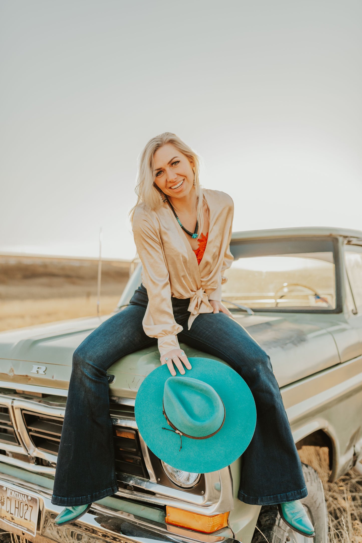 Woman sitting on old truck hood holding the TeePee Teal Cowgirl Hat by Charlie 1 Horse. 