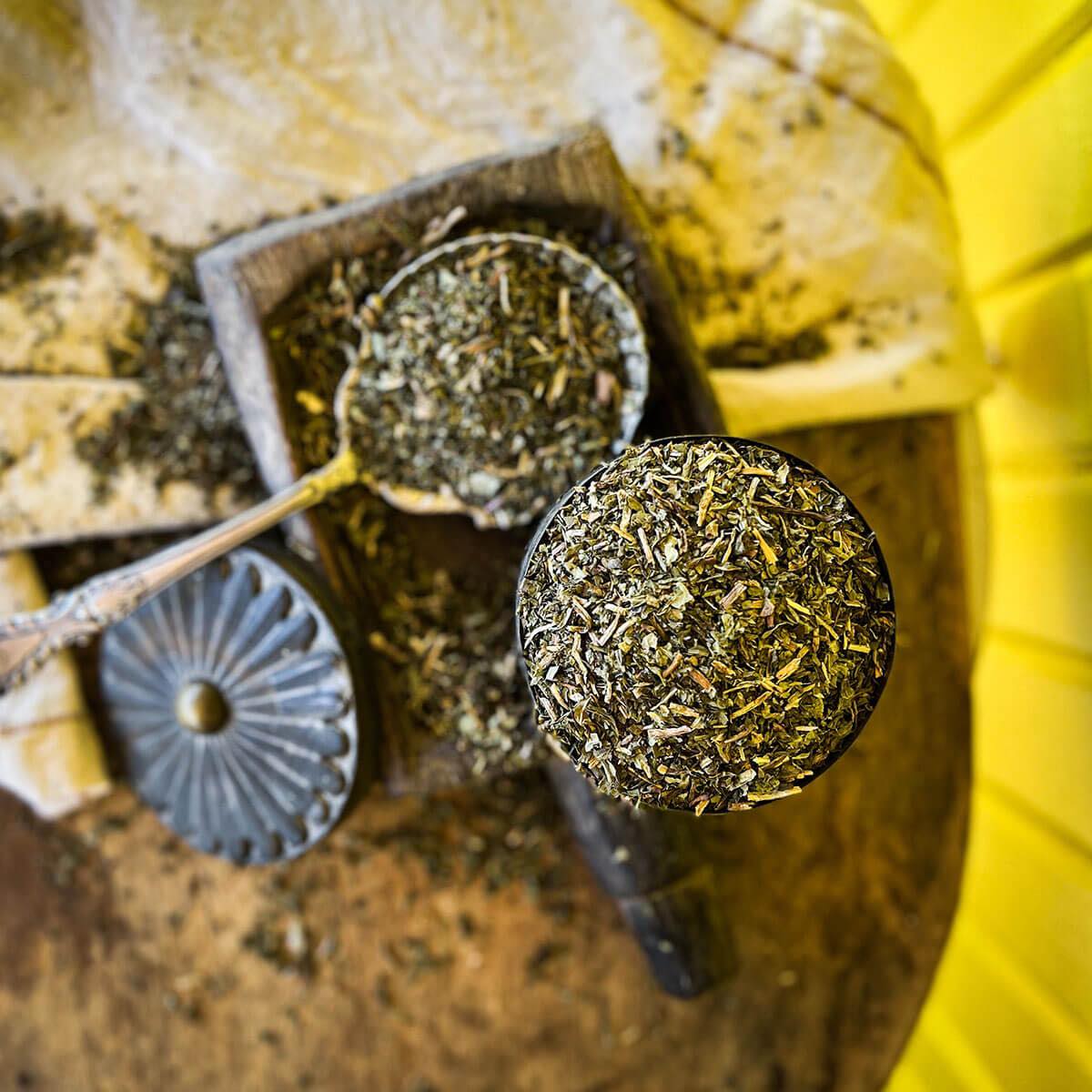 Dried dandelion leaf in a bowl with an overflowing silver spoon of the herb in the background.