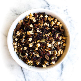 A white bowl filled with dried apple pie tea rests on a white marble tabletop.