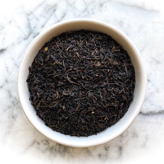 Dried black keemun tea in a white bowl on a white marble table.