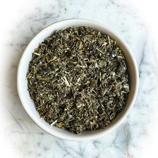 A white bowl filled with dried tea rests on a white marble surface.