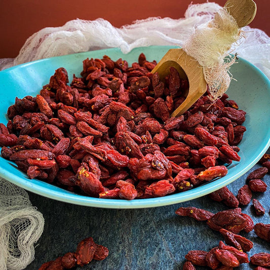 Dried goji berries in a blue bowl with a wooden scoop