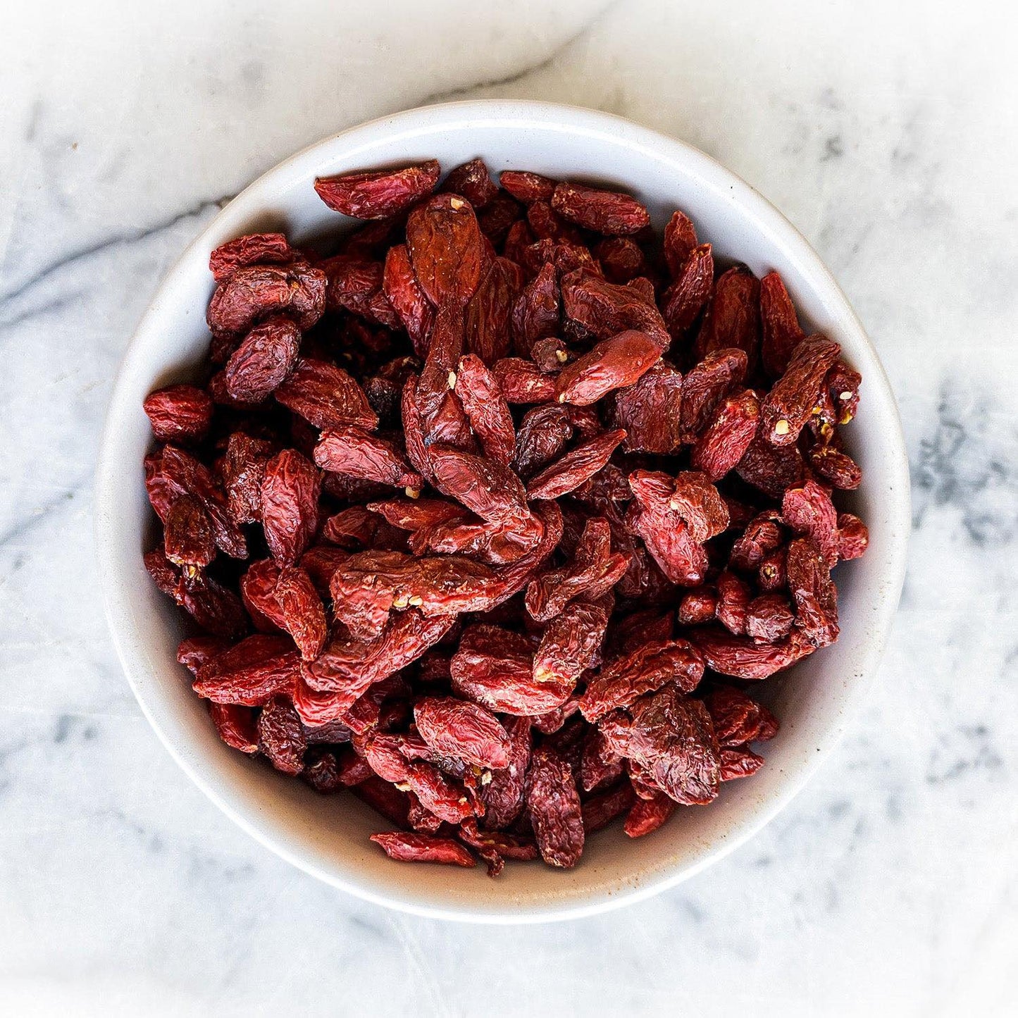 Dried goji berries in a white bowl on a white marble background